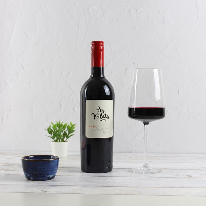 Bottle of Les Volets red wine with a glass on a white surface